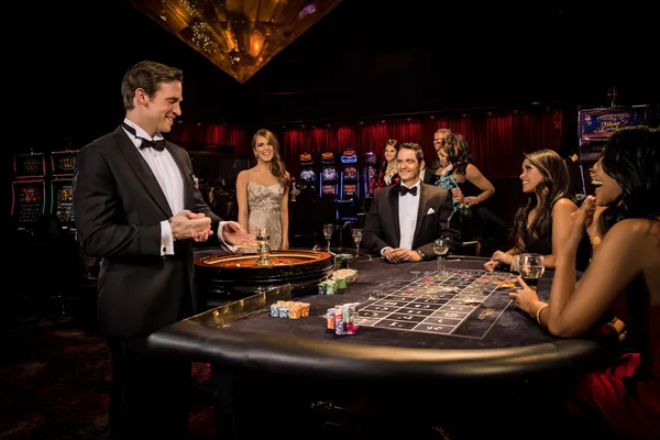 TAKSIM BET Canlı Casino — Gerçek krupiyelerle heyecan dolu masalara katılın Rulet masasında oyuncuları karşılayan smokinli profesyonel krupiye, TAKSIM BET’teki gerçek canlı casino hissini simgeler.